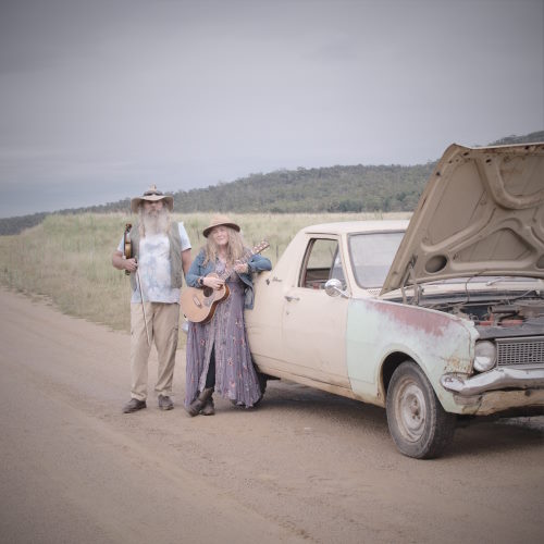 Photo of two performers standing in front of dead car