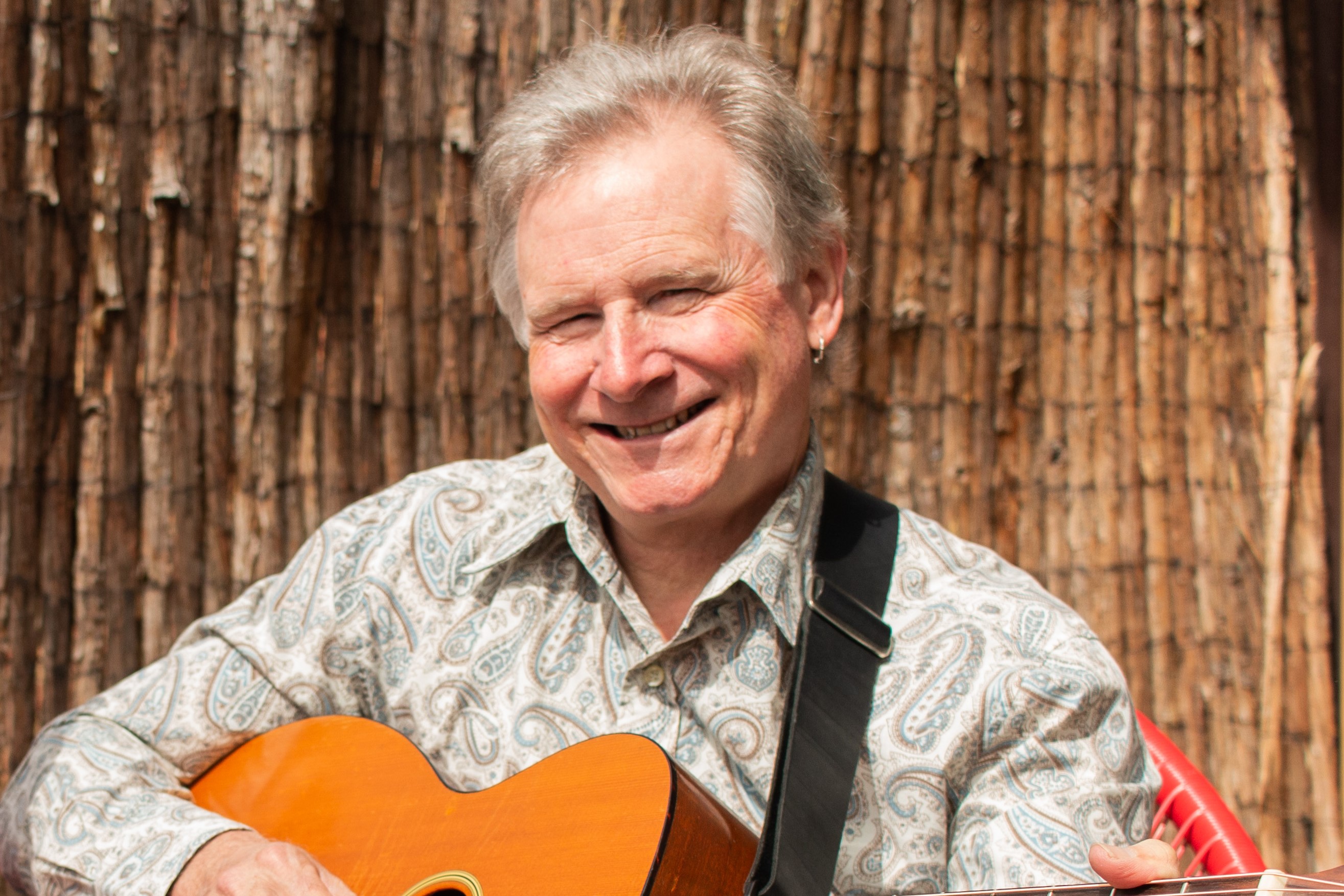 Photo of Peter Hicks smiling holding a guitar