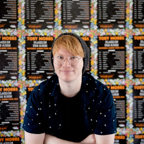 Toby Mobbs smiles from in front of his performance posters